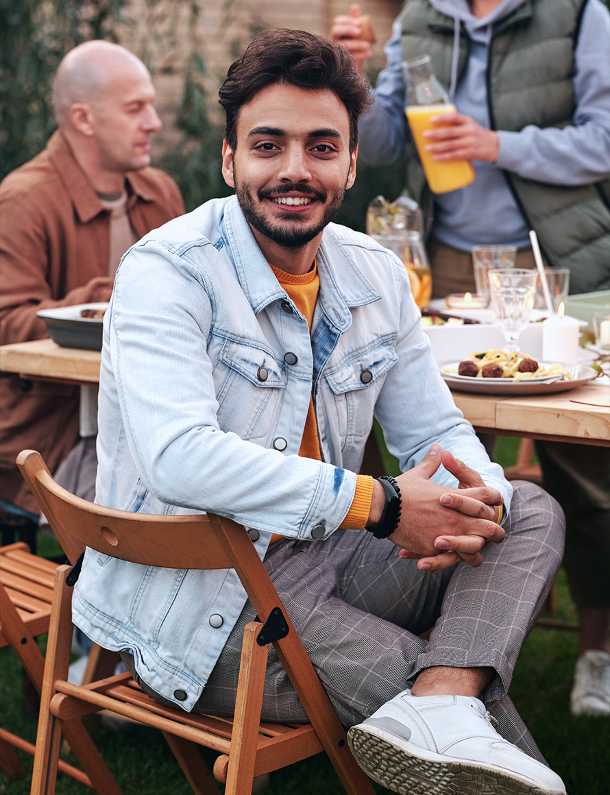 man in a light blue denim jacket is sitting in a chair with food on the table and smiling at the camera