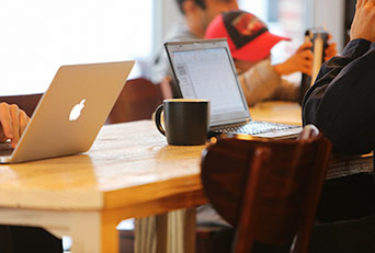 Two laptops open on a table. One person has a coffee cup.